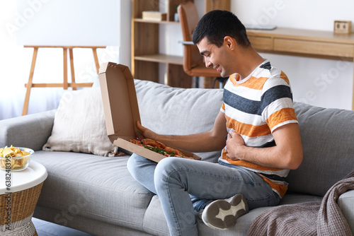 Young man with box of tasty pizza sitting on sofa at home