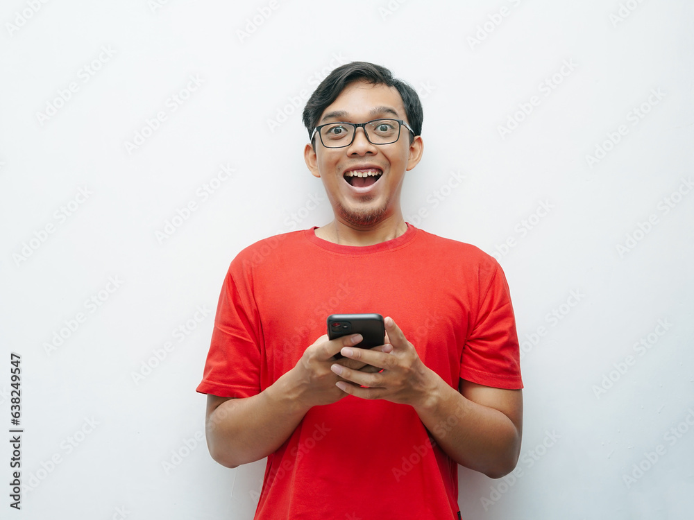 Portrait Indonesian Asian young man shocked looking at smartphone wears red t-shirt for August 17 Indonesia independence day concept Portrait Indonesian Asian young man shocked looking at smartphone wears red t-shirt for August 17 Indonesia independence day concept