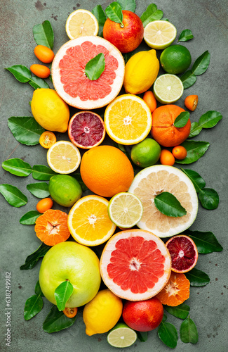 Colorful citrus fruits  food background  top view. Mix of different whole and sliced fruits  orange  grapefruit  lemon  lime and other with leaves on  green stone table