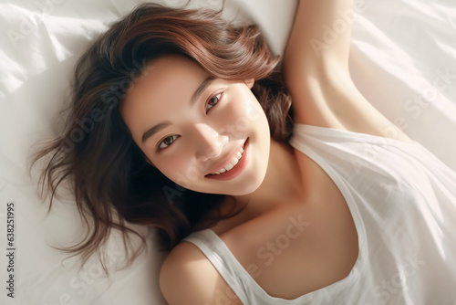 Pretty Asian young lady lies on indoor bed. She keeps eyes open and looks satisfied with positive thinking and smiling to camera. Generative AI. © Surachetsh