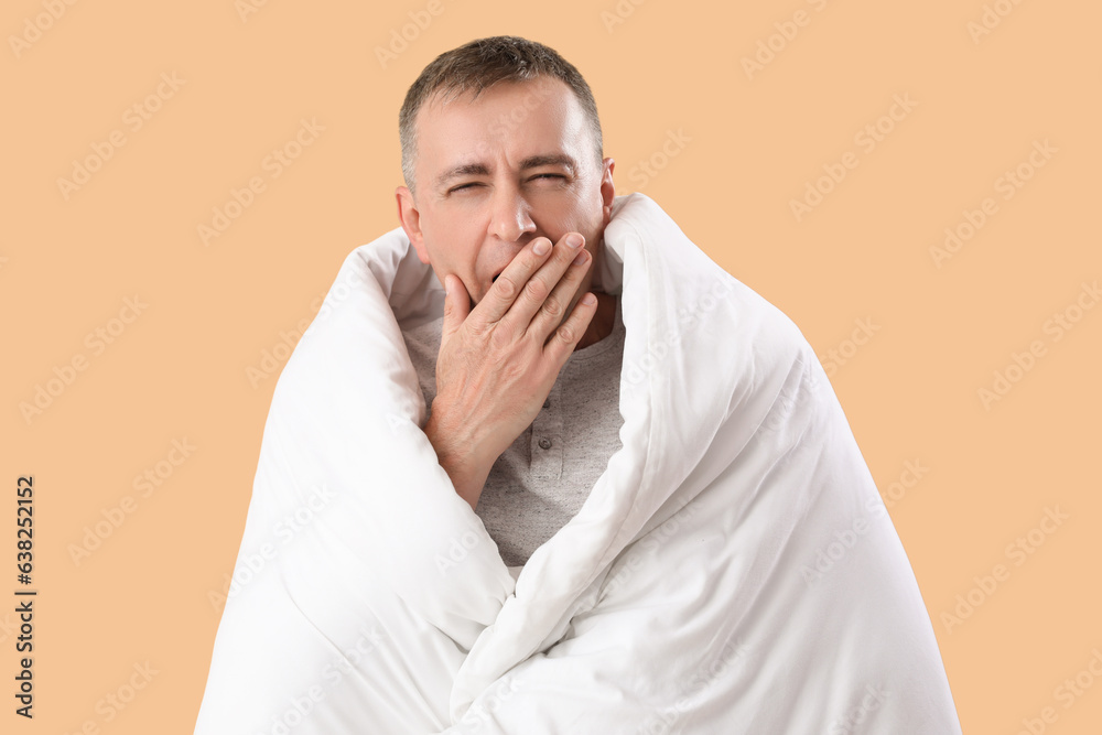Mature man with soft blanket yawning on beige background Mature man with soft blanket yawning on beige background