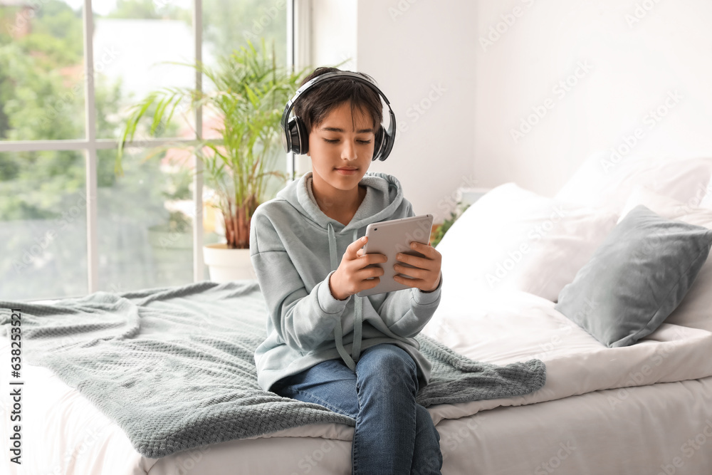Little boy with headphones using tablet computer in bedroom Little boy with headphones using tablet computer in bedroom