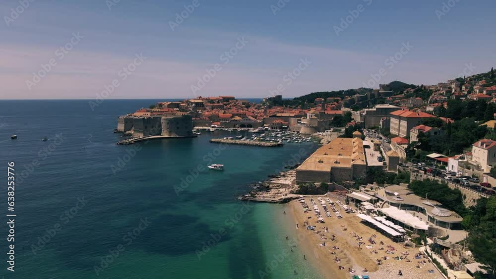 Aerial drone flying over Banje Beach and aqua blue waters towards the historic walled city of Dubrovnik, Croatia. Aerial drone flying over Banje Beach and aqua blue waters towards the historic walled city of Dubrovnik, Croatia.