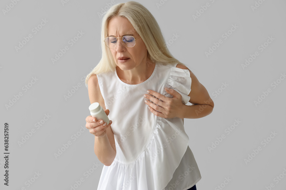 Mature woman with pill bottle having heart attack on grey background Mature woman with pill bottle having heart attack on grey background