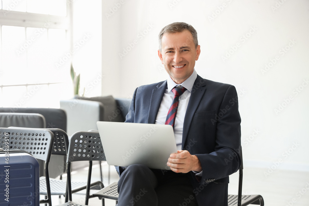 Mature businessman using laptop in hall of airport