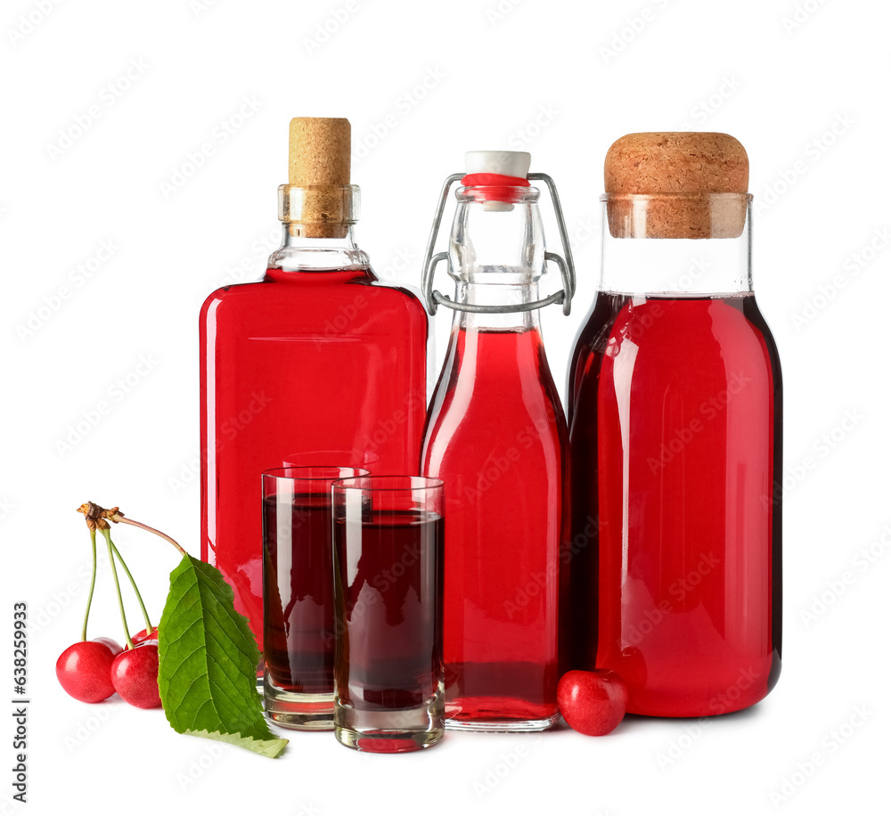 Glasses and bottles of sweet cherry liqueur with berries on white background