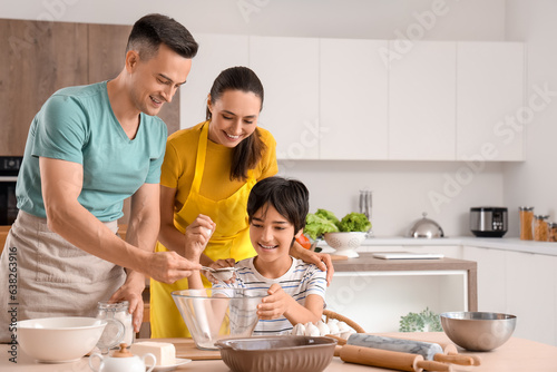 Happy parents with their little son preparing dough in kitchen