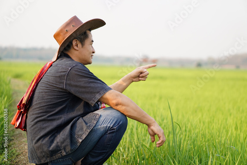 Handsome Asian man farmer sits at paddy field.point finger and look forward, feel relax. Concept, agriculture occupation, lifestyle. Copy space for adding text or advertisement. 