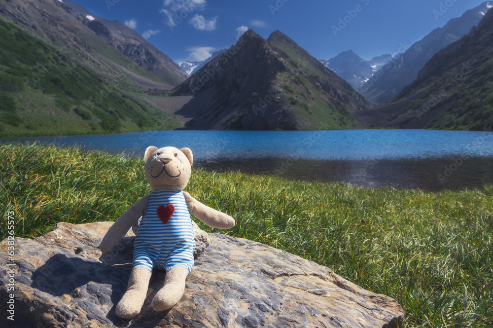 cute teddy bear traveler tourist resting by the lake in the mountains in summer in nature. Koksai Ainakol Lake in Tien Shan Mountains in Asia in Kazakhstan