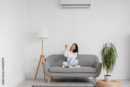 Beautiful Asian woman switching on air conditioner at home