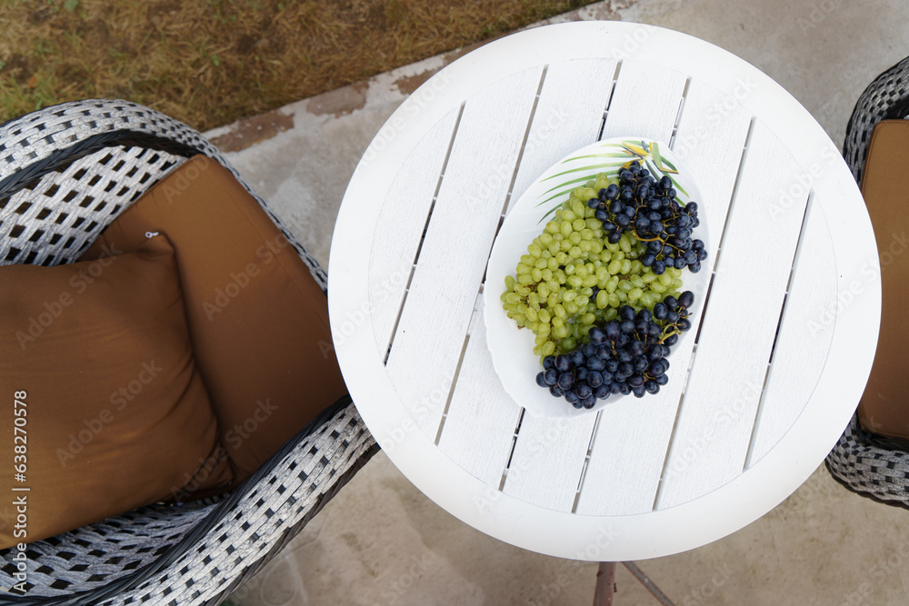 A dish with grapes stands on a white table, in the open air, in a summer cottage. - obrazy, fototapety, plakaty 