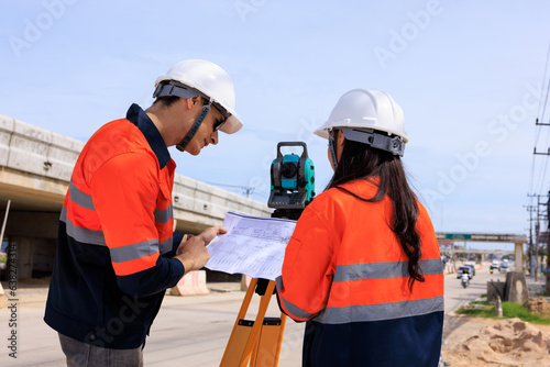 Engineer use theodolite equipment and looking blueprints construction project for route surveying to build a bridge across the intersection to reduce traffic congestion during rush hours