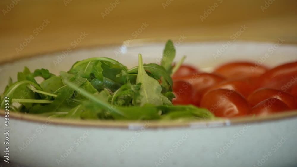 The girl puts green arugula in a plate with tomatoes The girl puts green arugula in a plate with tomatoes
