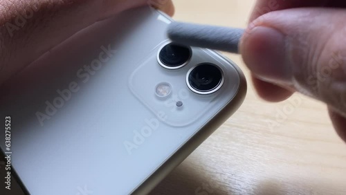 Hand using small tool brush to clean dust and dirt from phone camera lens. Disinfecting mobile phone concept. Male hand holding smartphone close up view on wooden table