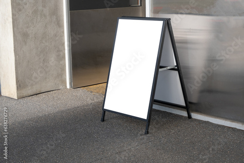 Side view of a blank white empty sandwich board placed at a half open door of a building entrance. Background texture of mockup template of outdoor ad signage easel. Copy space for your design.