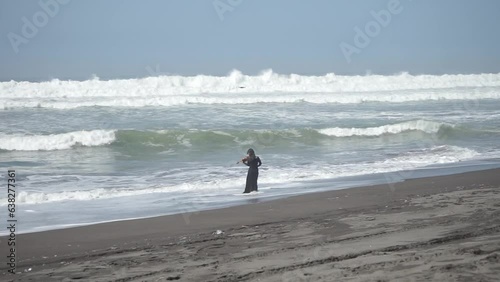 A woman in black dress playing violin on the beach facing the ocean waves photo