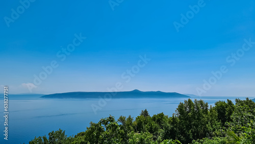 A view on the Mediterranean Sea from a viewpoint of Moscenice, Croatia. The slopes are overgrown with lush green plants. There is an island in the back. Clear and bright day. Summer holidays.