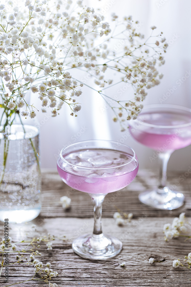 Obraz premium Pink cocktail placed on wooden board near the window with flowers as decoration. Great summer cocktail suggestion and party