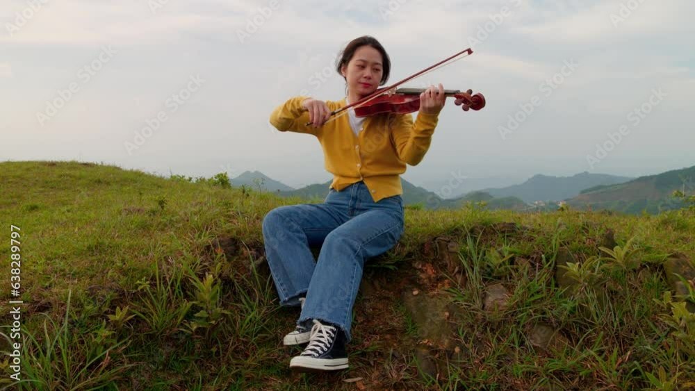 woman peacefully plays the violin outside while perched on an embankment, hair blowing in the wind woman peacefully plays the violin outside while perched on an embankment, hair blowing in the wind
