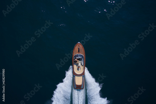 Top view of a wooden powerful motor boat. Luxurious wooden boat fast movement on dark water.Man and woman in luxury expensive wooden speedboat fast moving on dark water top view.
