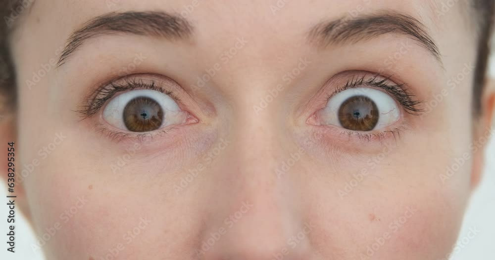 Close up, surprised woman eyes look at camera view, blink quickly on white background. Funny person surprise looking. Caucasian female wide open brown eyes, closeup. Young woman open eyes, shocked