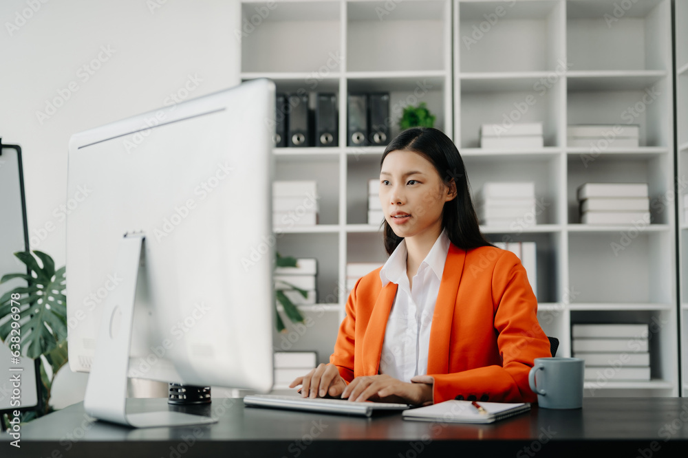 Young attractive Asian female office worker business suits smiling at camera with working notepad, tablet and laptop documents in office Young attractive Asian female office worker business suits smiling at camera with working notepad, tablet and laptop documents in office