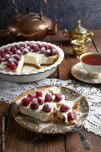 A piece of cheesecake decorated with raspberries on a porcelain plate.