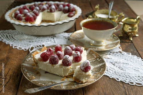 A piece of cheesecake decorated with raspberries on a porcelain plate.