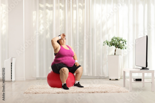 Tired overweight woman sitting on a fintess ball in front of tv