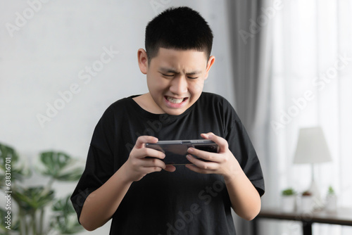 Asian boy playing games online with his smartphone, he mad feeling very angry on a sofa, games addict problem