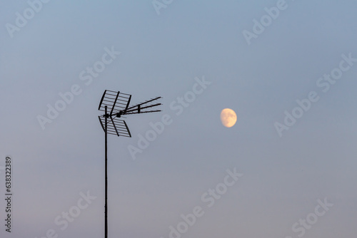 Antenna televisiva e luna nel cielo azzurro di sera. Fotografia orizzontale.