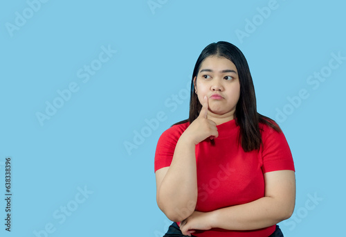 Portrait girl young woman asian chubby fat cute beautiful pretty one person wearing a red shirt is sitting, looking, and thinking idea  suspiciously and seriously  isolated blue background