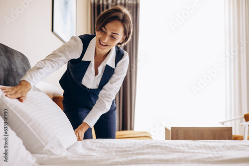 Woman housekeeper preparing bed cloths and pillows in the hotel room photo