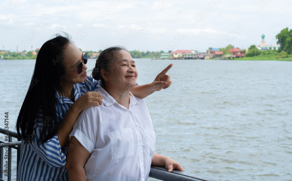Lovely and happy Asian granddaughter spending time with her grandmother in the river park on the weekend.