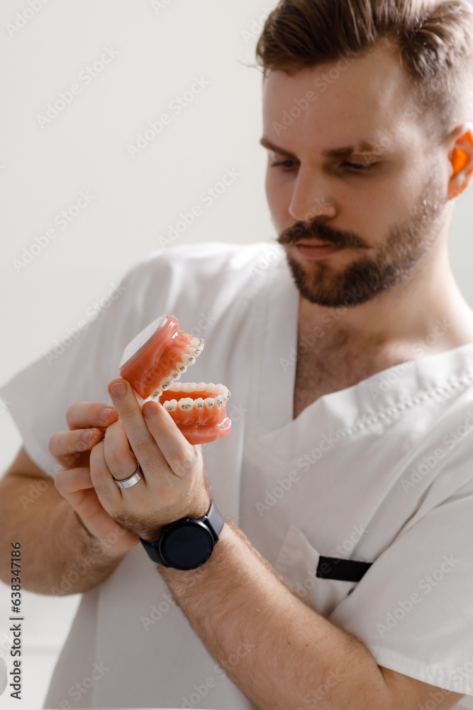 The dentist shows how to brush your teeth with a toothbrush on the layout of the jaw. Closeup of doctor's hands in gloves at work. Teeth model for demonstration.