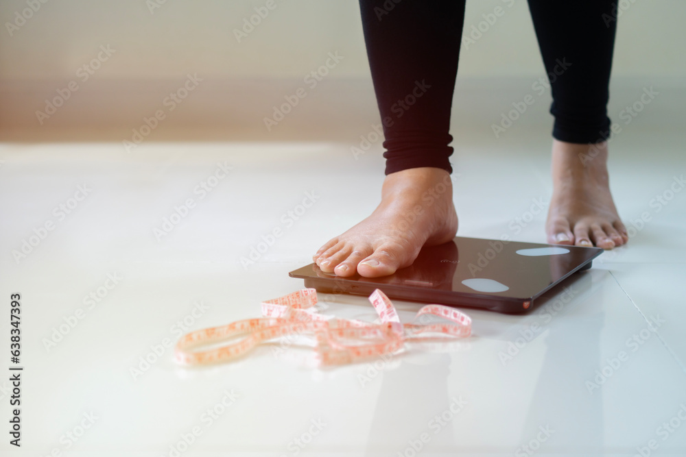 Unrecognizable young Asian woman stepping on scales to measure her weight at home.