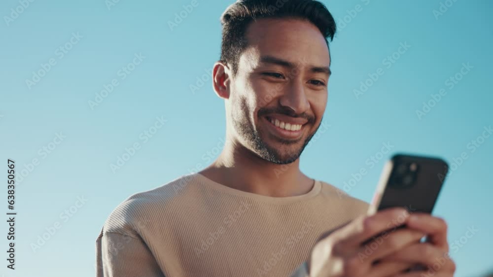 Blue sky, phone and young man typing a text message on social media, mobile app or website. Technology, online and happy Indian male person scroll on the internet with a cellphone for communication.