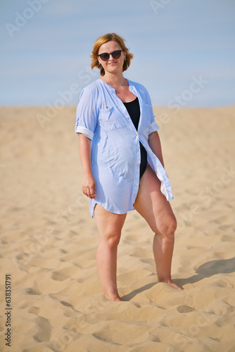 Woman in swimsuit  long shirt and sunglasses enjoying her summer holidays on the beach. Portrait of beautiful european woman enjoying summer sunny day.