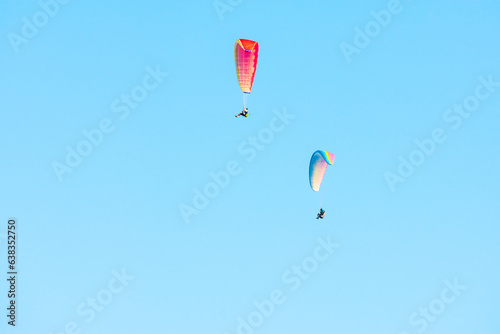 two colorful paragliders soaring through the blue sky