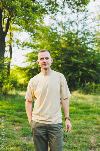 A handsome young man in a beige T-shirt and pants is walking on a green lawn. Relaxation in nature away from the city.