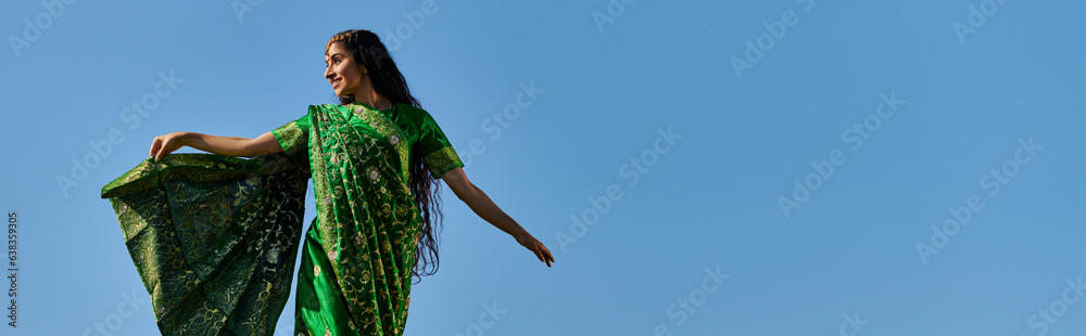 summer leisure, indian woman in sari smiling and looking away under blue cloudless sky, banner summer leisure, indian woman in sari smiling and looking away under blue cloudless sky, banner