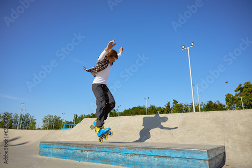 Tableau sur toile Young guy wearing inline skates doing balancing stunt at skateboard park