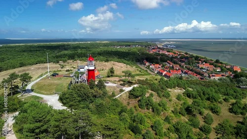 Aerial drone image of Vlieland. With bright red Lighthouse on top of a dune overlooking the small town, the North Sea and the Wadden Sea on a bright summer day. High quality stock film photo