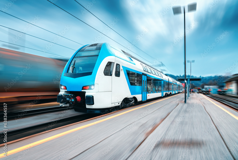 High speed train in motion on the railway station at sunset. Blue modern intercity passenger train with motion blur effect on the railway platform. Railroad in Europe. Commercial transportation