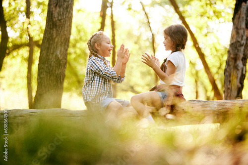 Playful happy children, girls sitting on log, playing, having good time in forest on sunny day. Concept of leisure activity, childhood, summer, friendship, active lifestyle, fun, nature #638364501