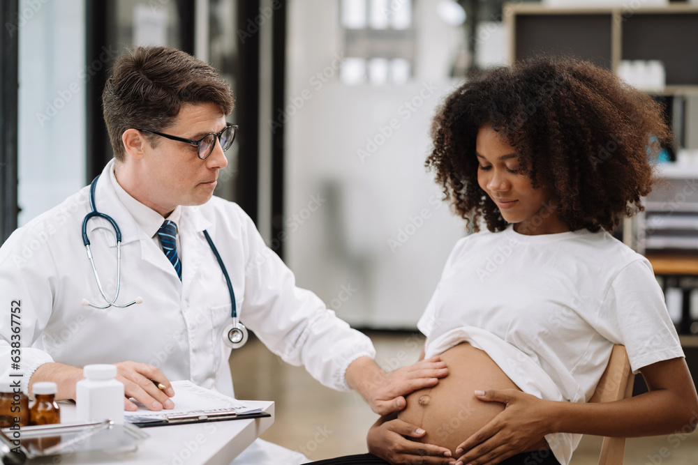 Fototapeta premium Happy pregnant woman has appointment with doctor at clinic. male medic specialist with stethoscope listens to baby's heartbeat in mother's belly. Pregnancy, health care concept.