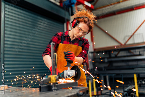 A self-employed worker is cutting a metal beam using a grinder, she is focused on her work and wearing protective gear