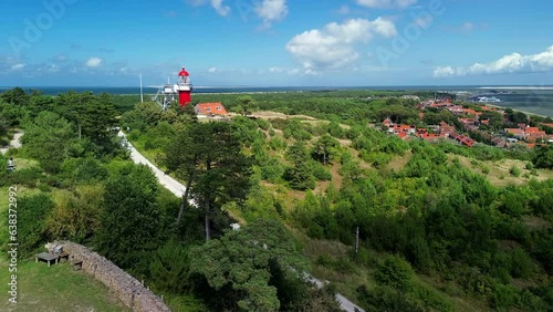 Aerial drone image of Vlieland. With bright red Lighthouse on top of a dune overlooking the small town, the North Sea and the Wadden Sea on a bright summer day. High quality stock film photo