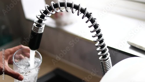 Person filling glass by tap water. Holding glass under running faucet.  Ecological and healthy drink. close up