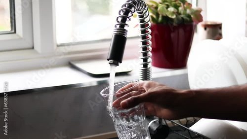 Person filling glass by tap water. Holding glass under running faucet.  Ecological and healthy drink, wide angle one hand